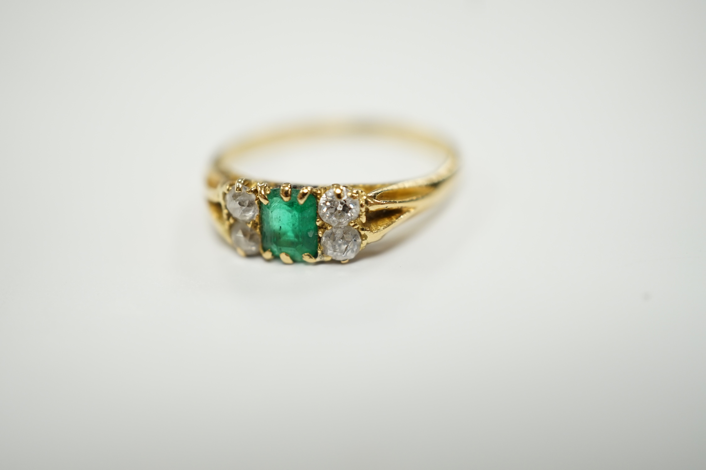 An 18ct, single stone emerald and four stone diamond cluster set ring, size M, gross weight 2.2 grams.